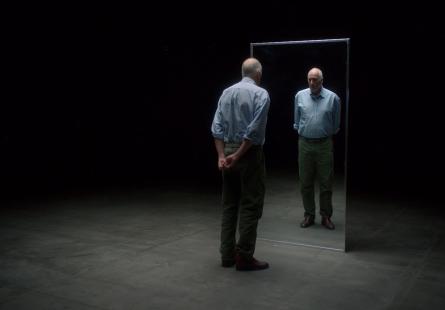 Senior white man with back to camera looking into mirror